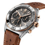 The Breitling Chronomat B01 42 Triumph is a chronograph watch with a brown leather strap and a black dial featuring gold accents.