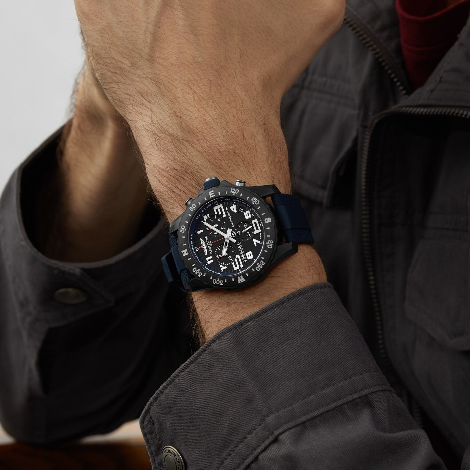 A person in a dark jacket showcases the Breitling Endurance Pro 38, an athleisure watch featuring a black analog dial, multi-function features, and bold white markings.
