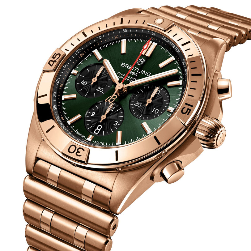 The Breitling Chronomat B01 42 is a gold mechanical chronograph wristwatch with a green dial, three black subdials, and a matching gold metal bracelet.