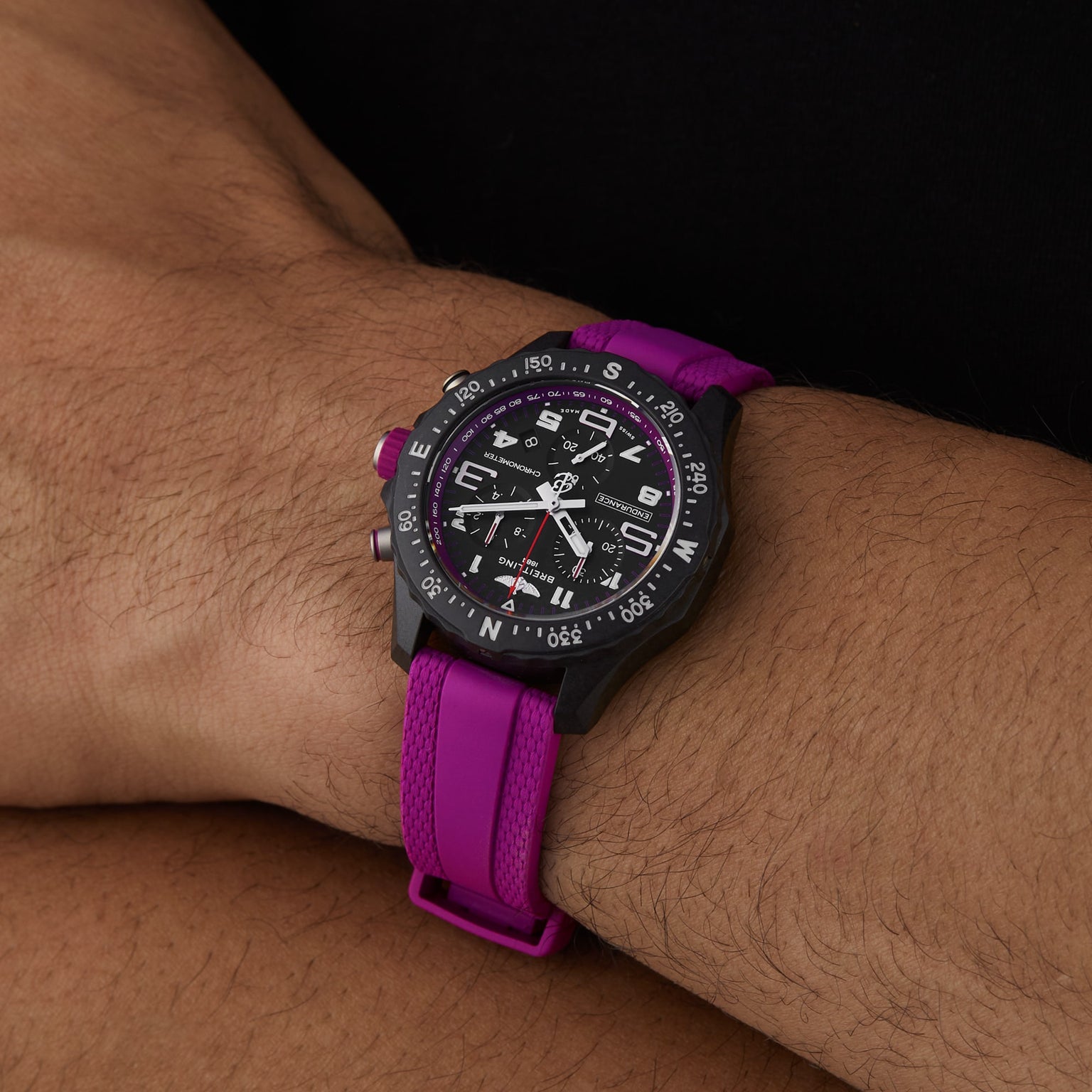 A person wearing the Breitling Endurance Pro 38, an athleisure watch featuring a black analog dial, pink strap, and a bezel marked with compass directions.