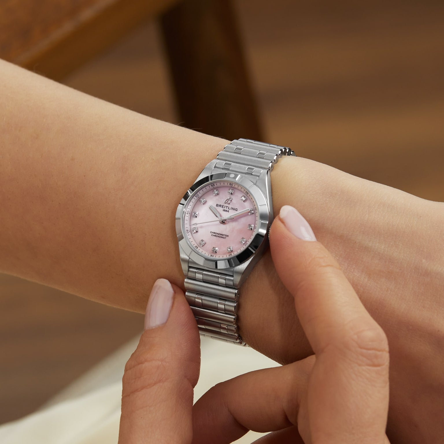 A person wearing a Breitling Chronomat 28 silver wristwatch with a pink dial, adjusting the time.