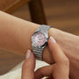 A person wearing a Breitling Chronomat 28 silver wristwatch with a pink dial, adjusting the time.