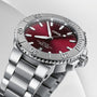 A close-up of the Oris Aquis Date Relief, a stainless steel wristwatch with a red dial, silver bezel, time set to 10:10, and a date display at the 6 o’clock position.