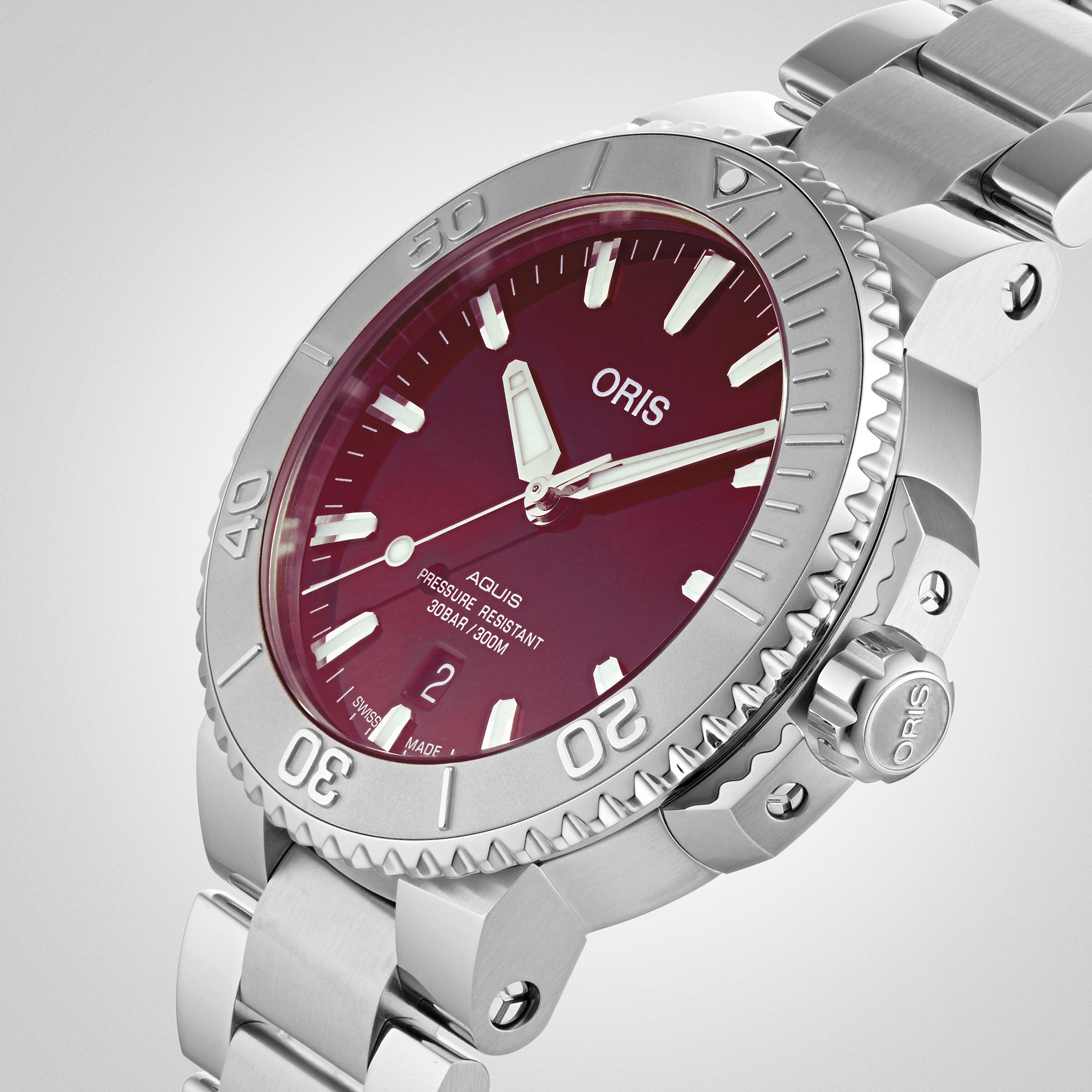 Close-up of the Oris Aquis Date Relief wristwatch in stainless steel, featuring a burgundy dial, silver bezel, metal bracelet, and date display at six o’clock.