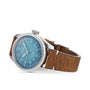 A professional pilot’s watch, the Oris Big Crown Oris X Cervo Volante displays a blue dial, white numerals, and a brown leather strap, elegantly positioned on its side against a white background.