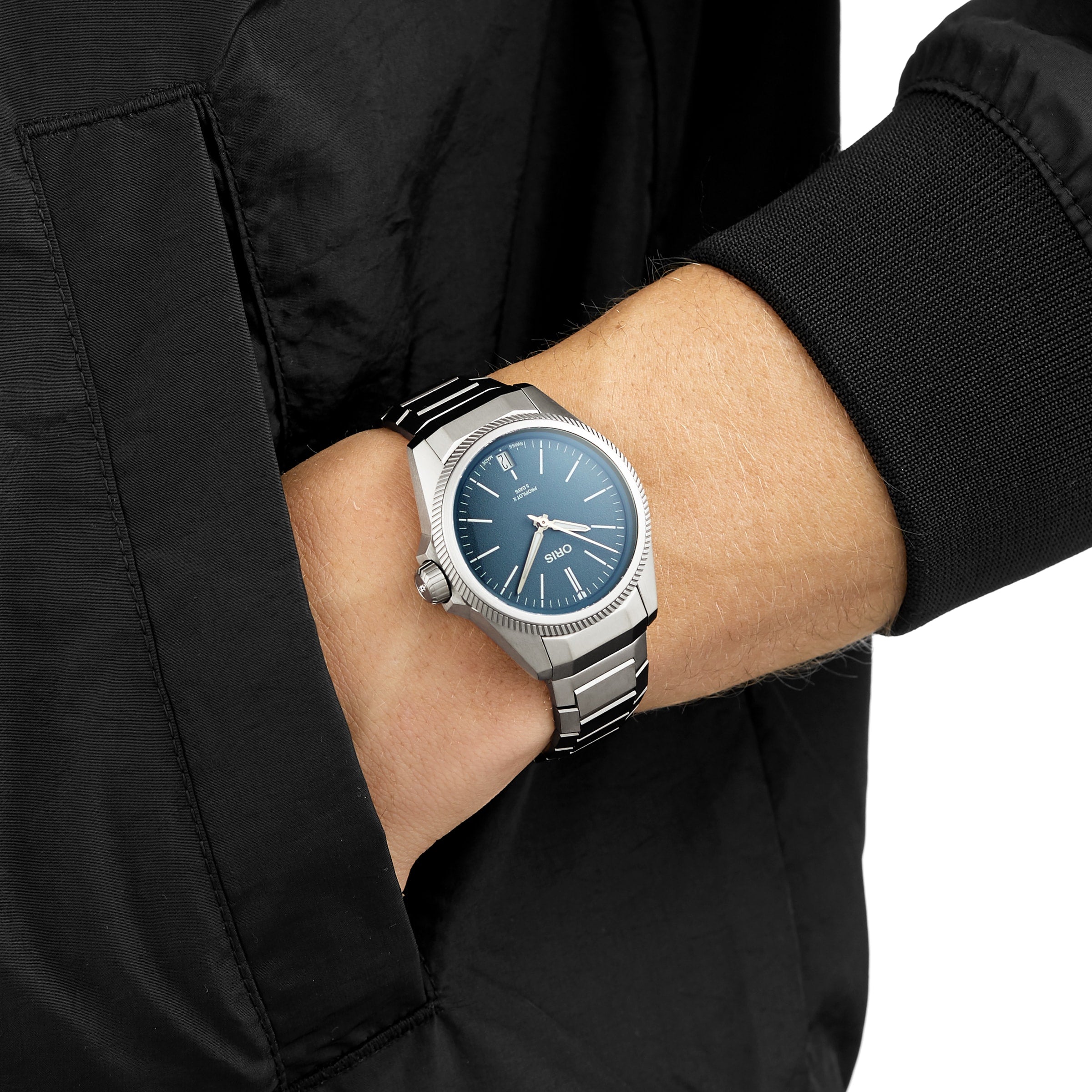 A person wearing an Oris ProPilot X Calibre 400 watch with a titanium case and blue dial rests their hand in the pocket of a black jacket, highlighting its aviation heritage style.