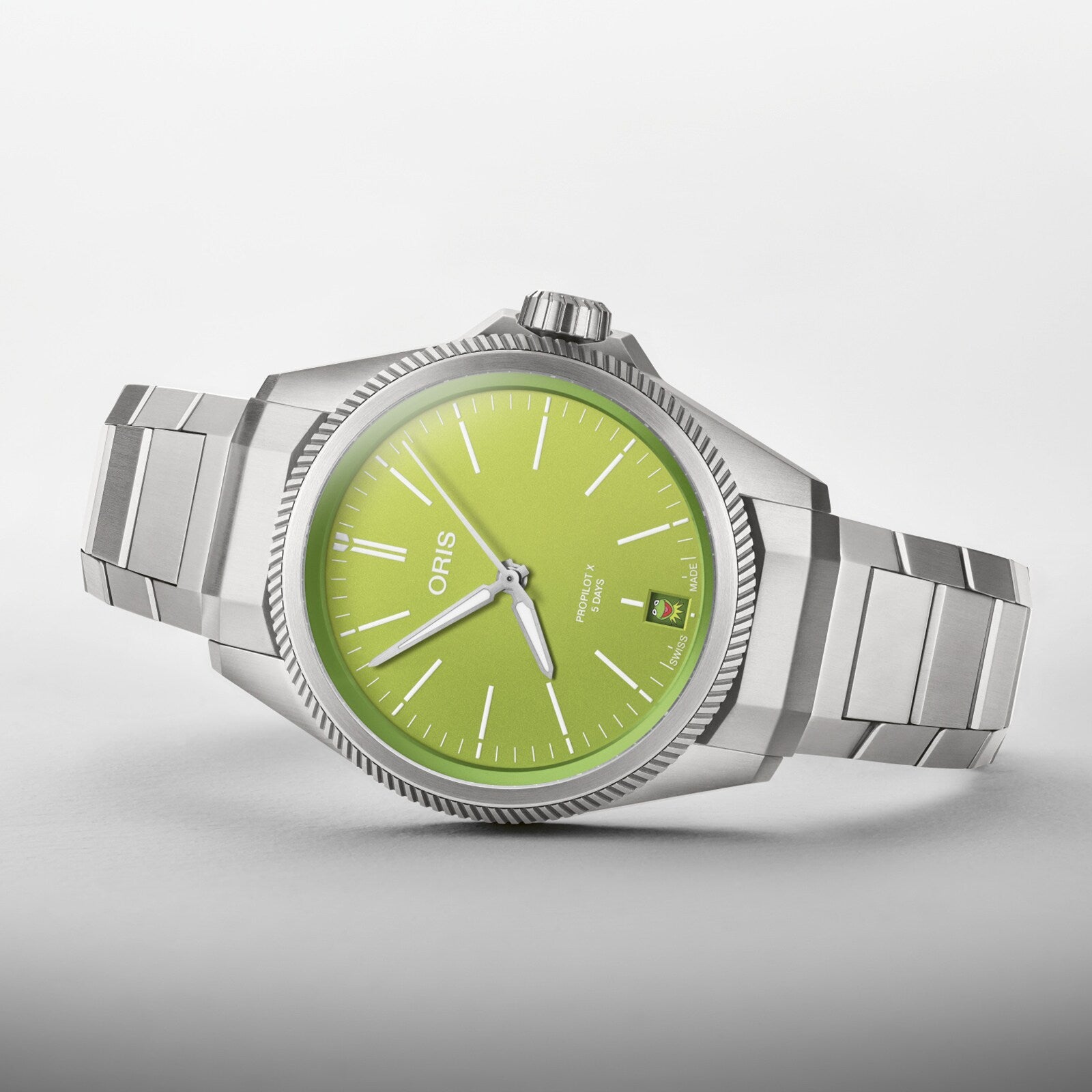 The Oris ProPilot X Kermit Edition features a stainless steel case, lime green dial, silver hour markers, date window, and metal link bracelet, showcased against a plain background and inspired by Kermit the Frog.