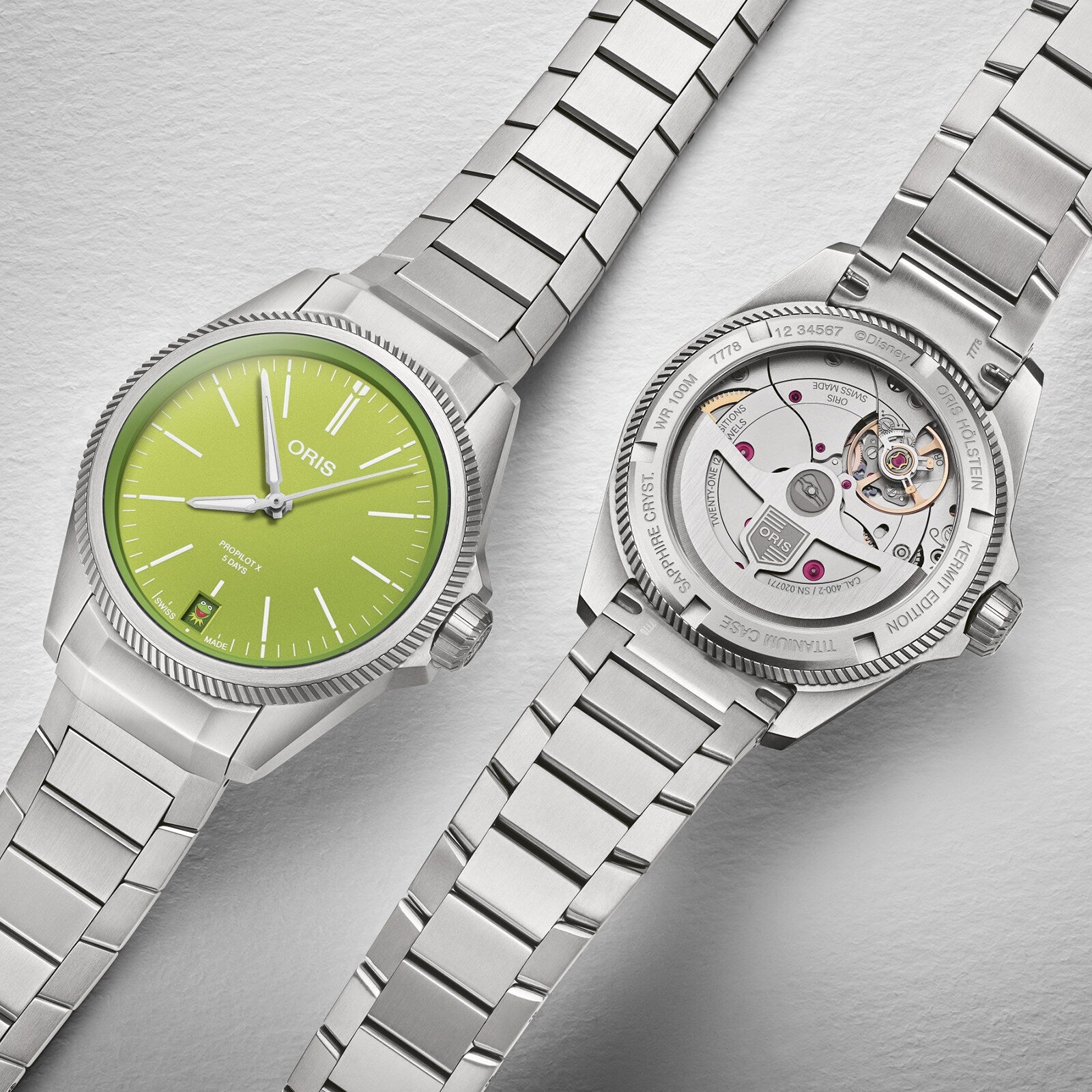 Two Oris ProPilot X Kermit Edition stainless steel wristwatches are shown: one displays a green dial, while the other reveals its Oris Calibre 400 movement through a transparent case back.
