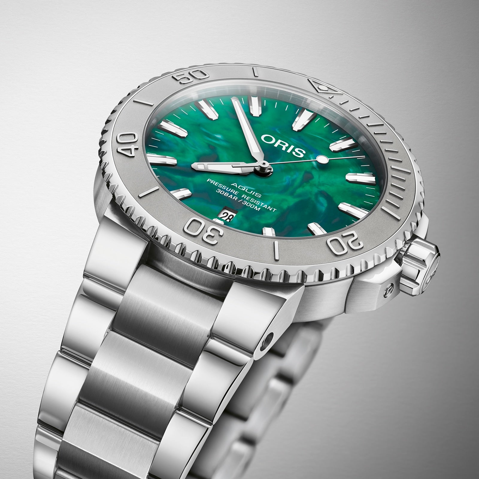 The Oris Aquis Oris X Bracenet watch features a stainless steel case, green mother-of-pearl dial, bold markers, rotating bezel, and date window—crafted with upcycled ghost fishing nets—shown on a gradient backdrop.