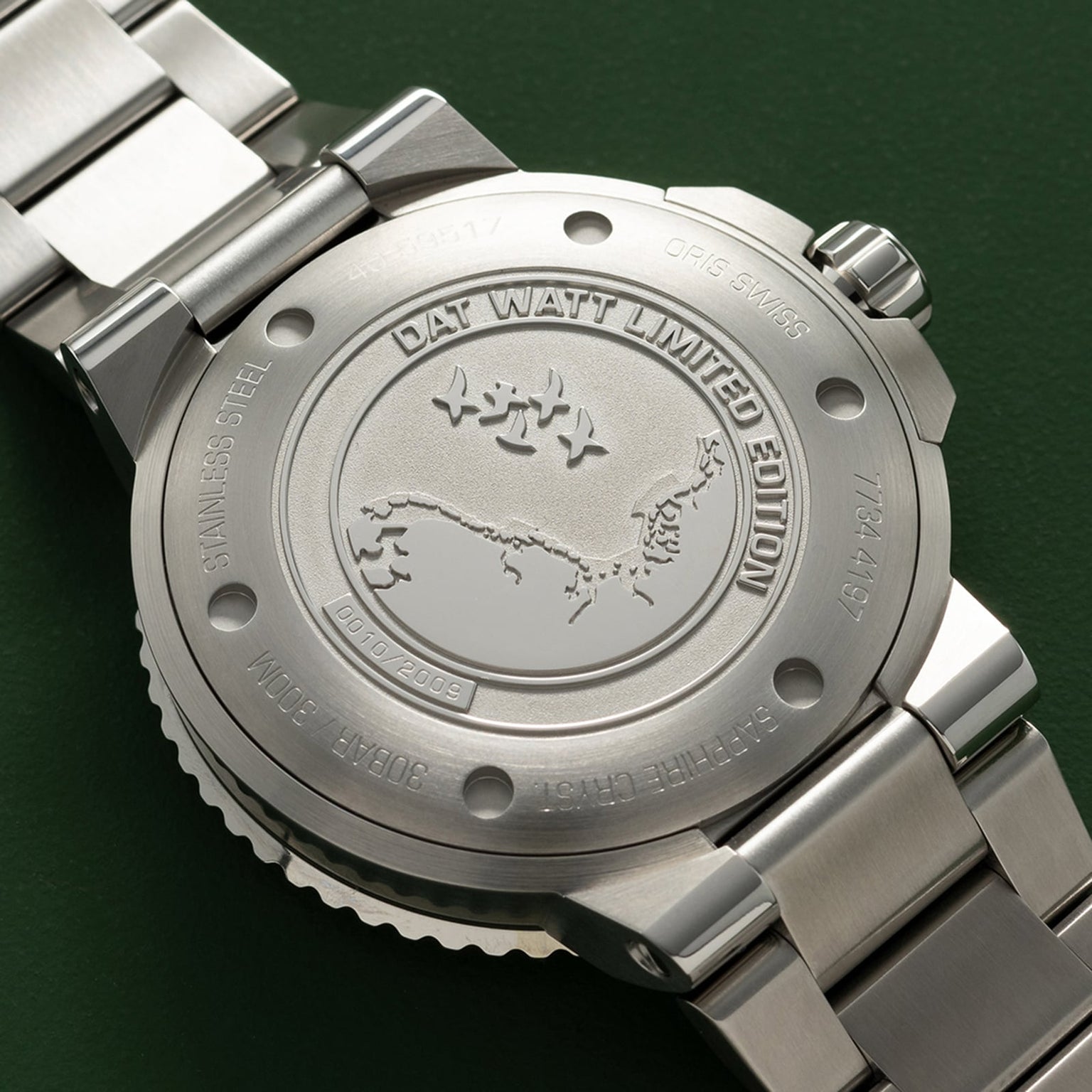 Close-up of the back of the Oris Dat Watt Limited Edition II watch, crafted in stainless steel and engraved with DAT WATT LIMITED EDITION plus a Wadden Sea-inspired map, shown against a green background.