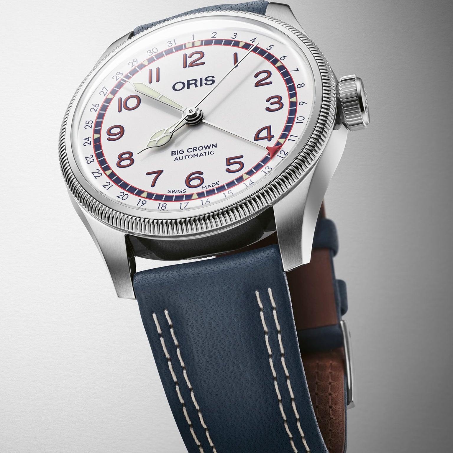 An Oris Big Crown Hank Aaron Limited Edition wristwatch with a white dial, red numerals, and blue leather strap shown at an angle in its signature stainless steel case against a light background.
