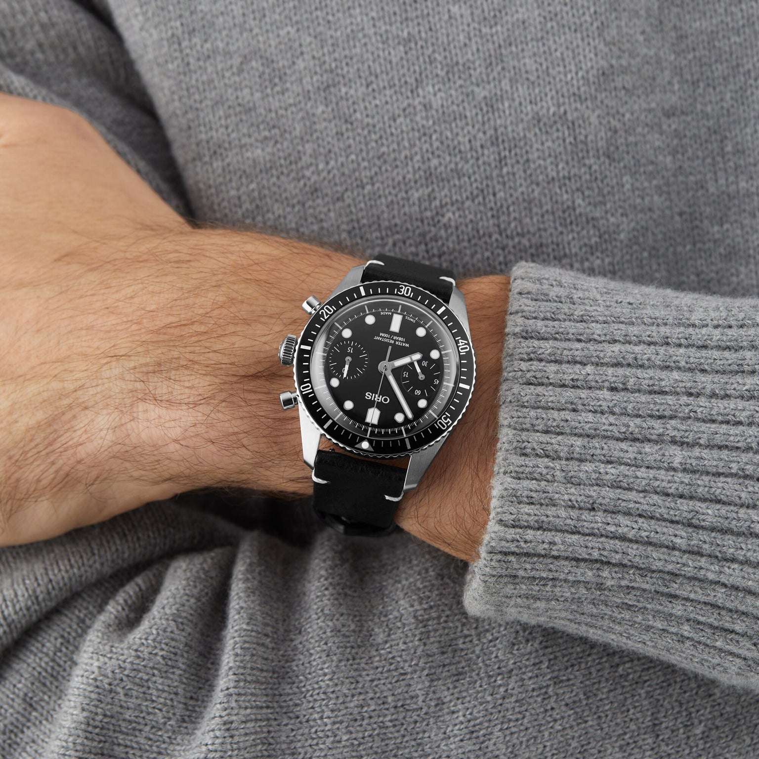 A person wearing an Oris Divers Sixty‑Five Chronograph watch and a gray sweater.