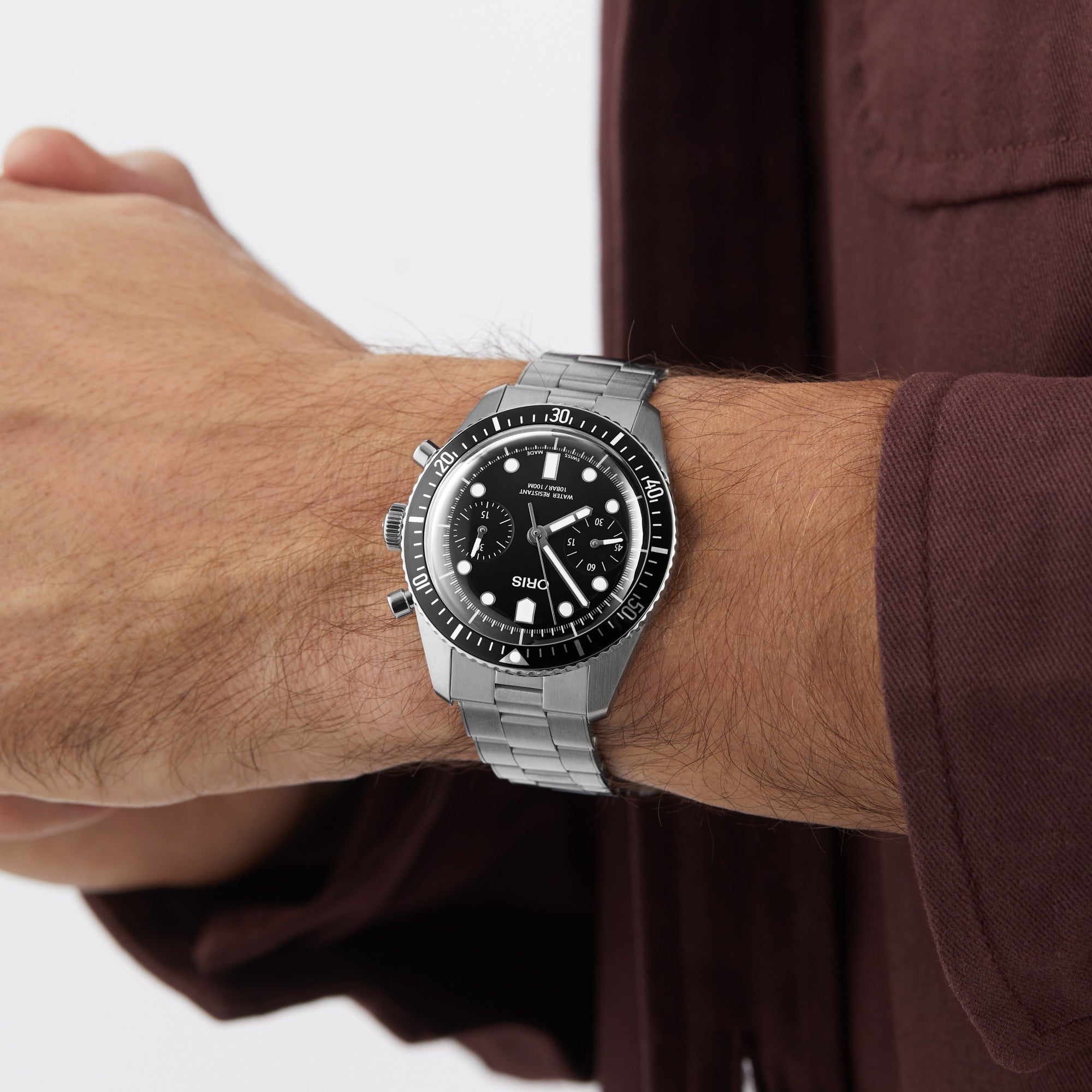 A person wearing the Oris Divers Sixty‑Five Chronograph with a black dial and a maroon long-sleeve shirt.