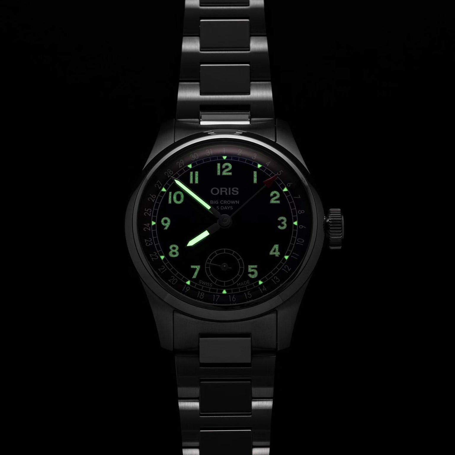 A black metal Oris Big Crown Pointer Date Calibre 403 wristwatch with luminous green numerals and hands is displayed in a dark setting, its midnight blue dial highlighting the brand’s signature automatic movement.
