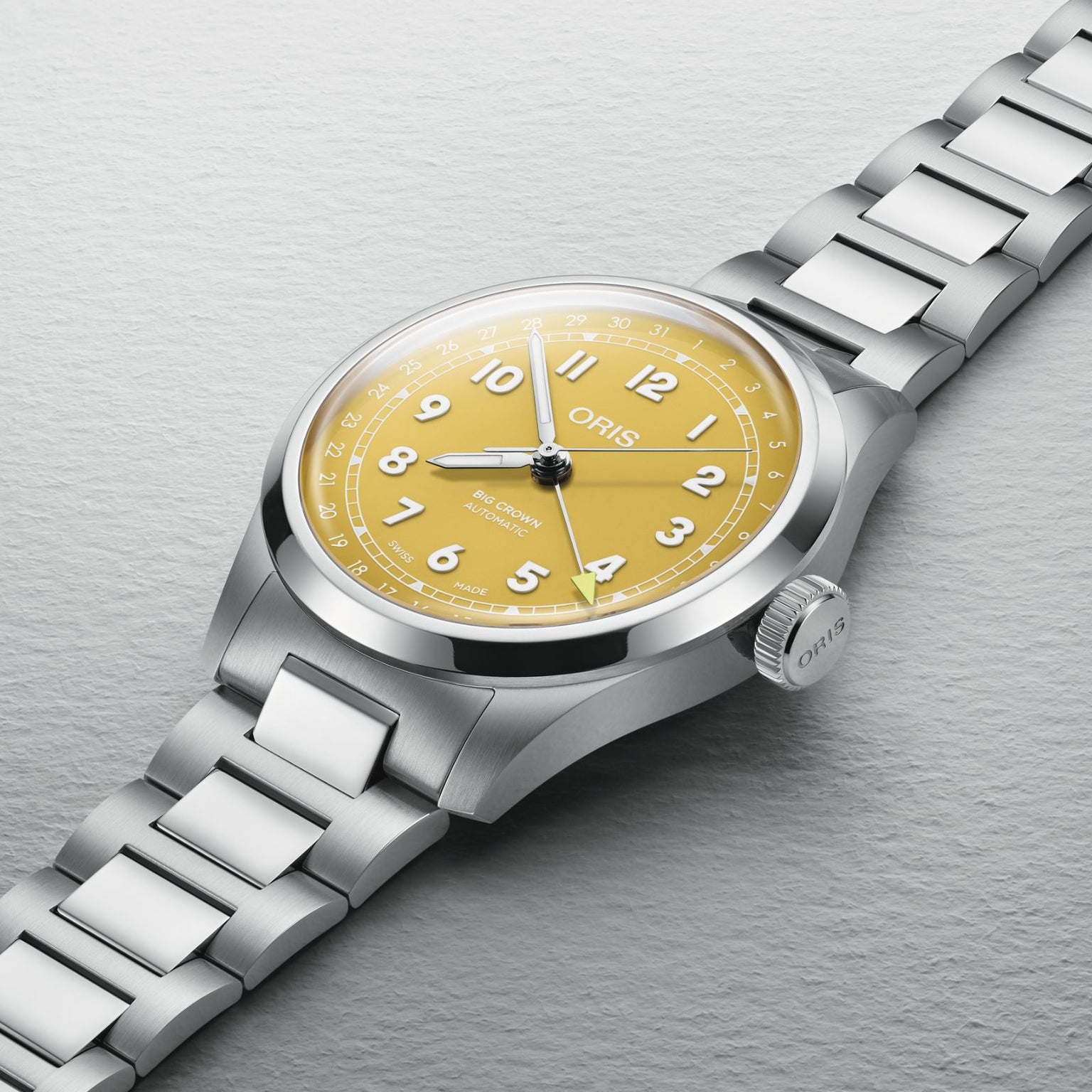 The Oris Big Crown Pointer Date is a stainless steel wristwatch with a sunshine yellow dial, white numerals, and silver hands on a metal bracelet, shown against a light gray background.