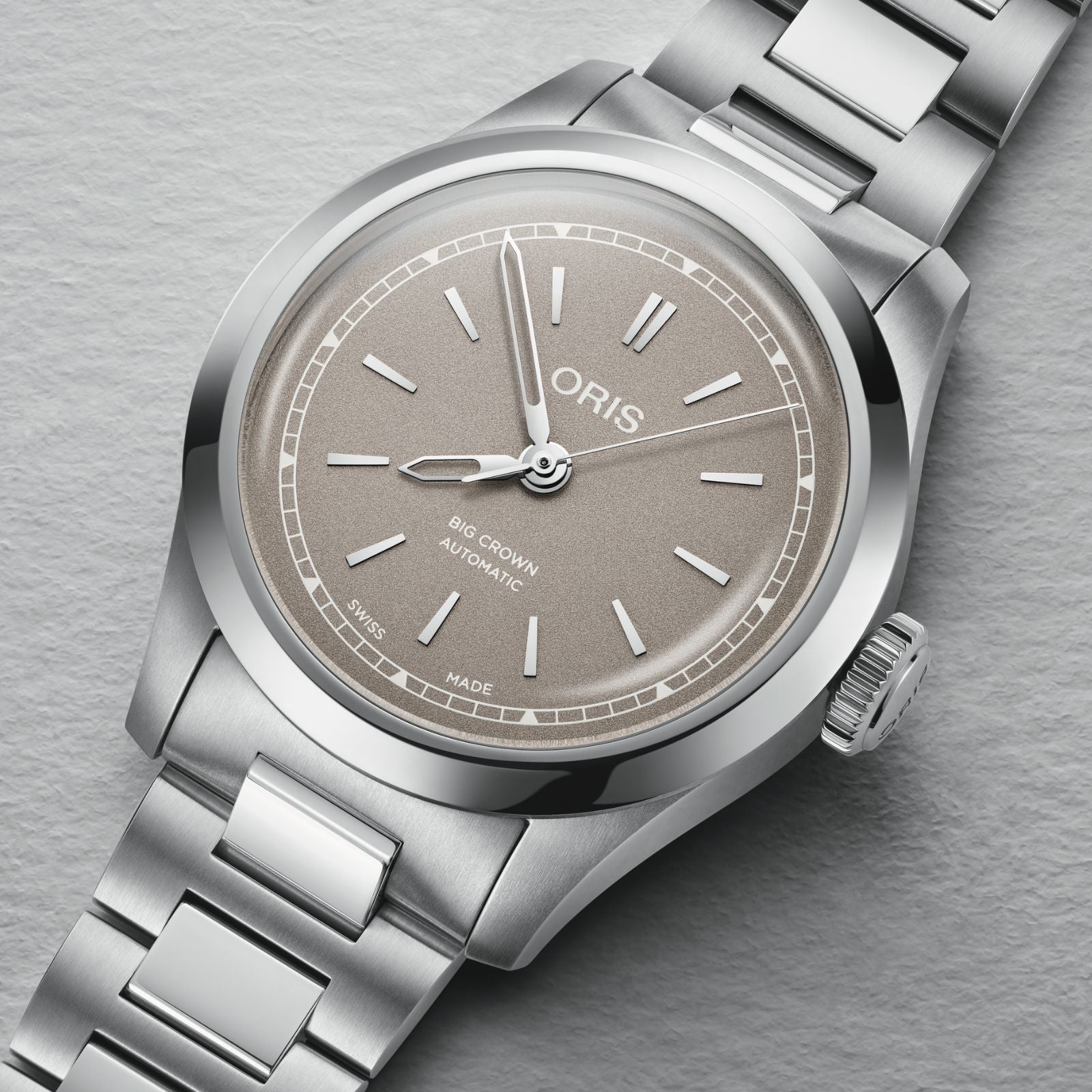 The Oris Big Crown is a Swiss Made automatic watch with a stainless steel case, beige dial, silver markers and hands, date at 6 o’clock, and a metal bracelet.