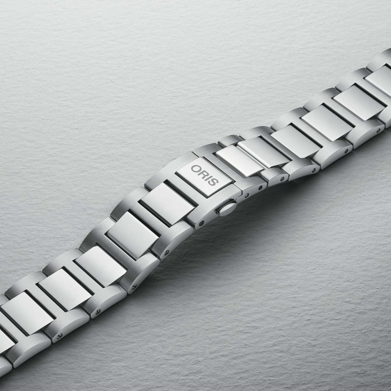 A close-up of an Oris Big Crown watch bracelet featuring polished and brushed silver links on a light gray surface.