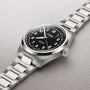 Silver-tone watch with black dial, large Arabic numerals, date window, and matching metal bracelet.