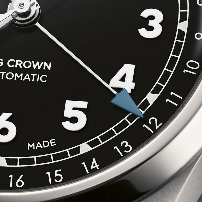 Watch face with black dial, white Arabic numerals, blue pointer hand, date window, and tachymeter scale on silver case.