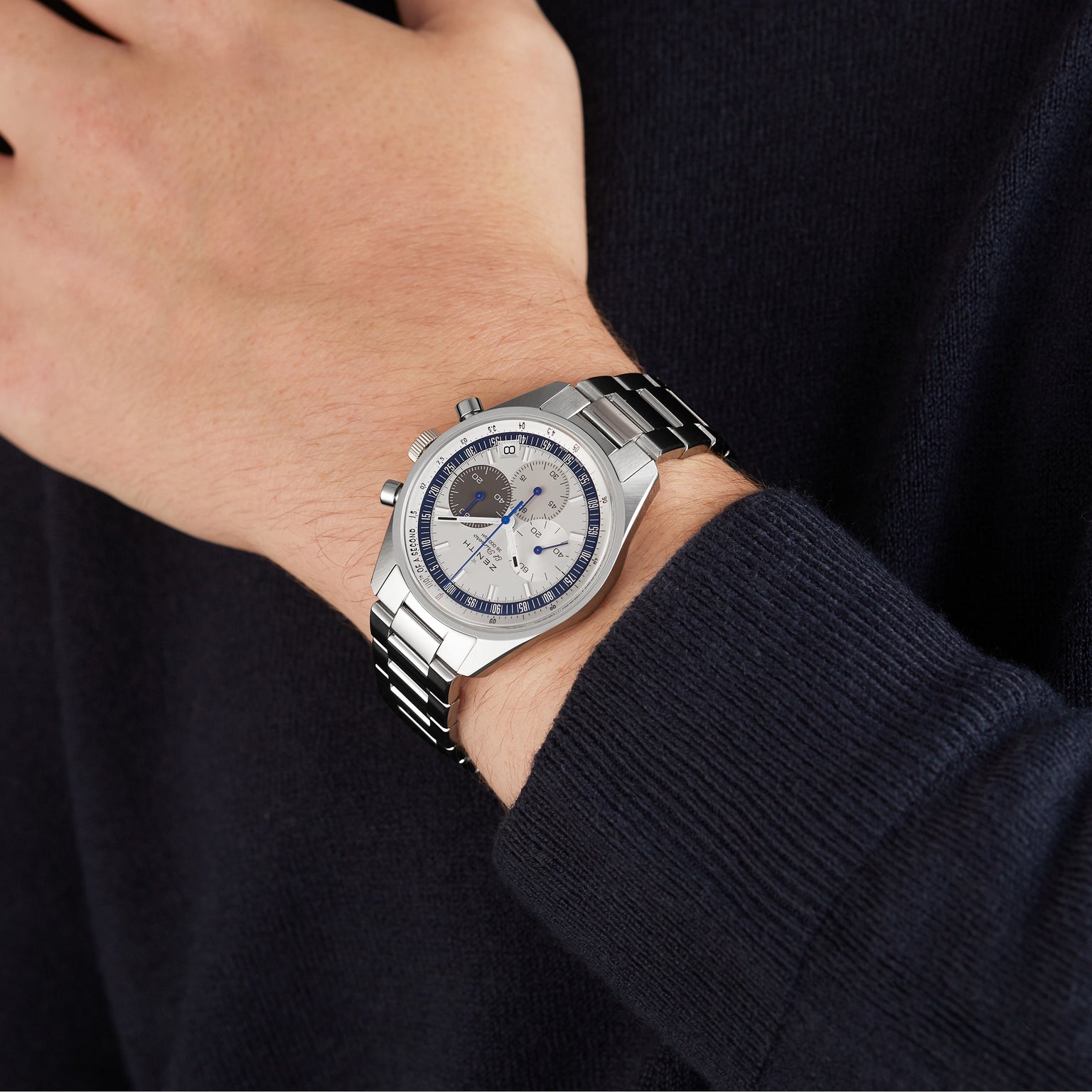 A person wearing the Zenith Limited Edition WOSG Exclusive Chronomaster EP Original, a silver wristwatch with a blue and white dial, multiple subdials, and the precise El Primero 3600 automatic chronograph on their left wrist.