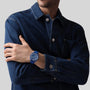 A person in a dark denim jacket crosses their arms, showing a Zenith Limited Edition Pilot Big Date Flyback 160th Anniversary Edition on their left wrist against a plain gray background.