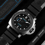 A close-up shows the Panerai Submersible men's dive watch with a black dial, 42mm stainless steel case, blue accents, and black rubber strap next to branded Panerai packaging and accessories.