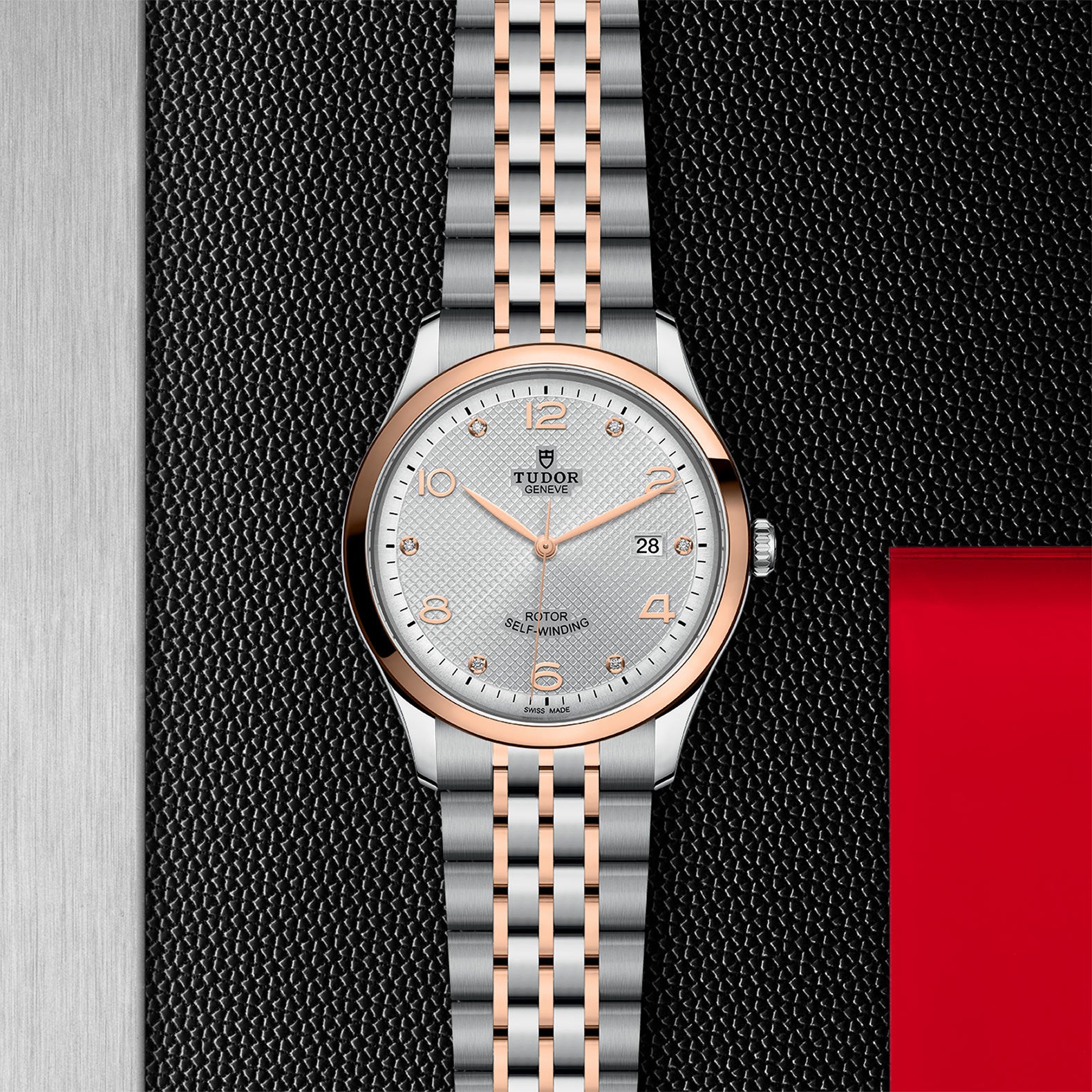 The TUDOR 1926 wristwatch features a silver and rose gold two-tone metal band, white dial with gold hour markers, date display, and self-winding movement, shown against a textured black background.