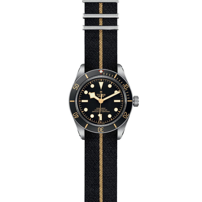 The TUDOR Black Bay 58 is inspired by classic diving watches, featuring a black dial with beige markers, a black fabric strap with a beige stripe, and a black bezel with gold markings, all echoing traditional mechanical movement style.