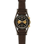 The TUDOR Black Bay Chrono S&G wristwatch features a brown leather strap, black dial, gold subdials, and gold pushers, displayed against a white background.