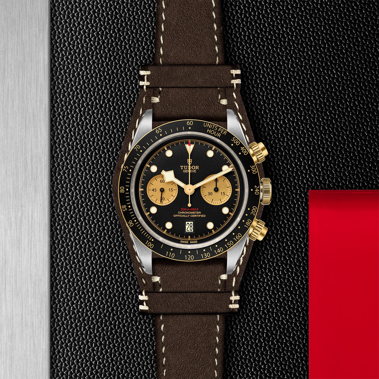 The TUDOR Black Bay Chrono S&G, featuring a black and gold dial, brown leather strap, and tachymeter bezel, is displayed on a textured black and metallic background.