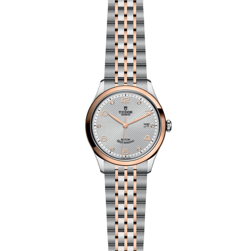 The TUDOR 1926 features a silver and rose gold case, metal link bracelet, round face, date at 3 o’clock, and dot hour markers on a textured silver dial—ideal for fans of classic mechanical watches.