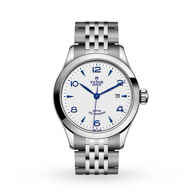 The TUDOR 1926 wristwatch features a silver case, white textured dial with blue markers, a date window at 3 o’clock, and is displayed on a metal link bracelet against a white background—an elegant classic from TUDOR.