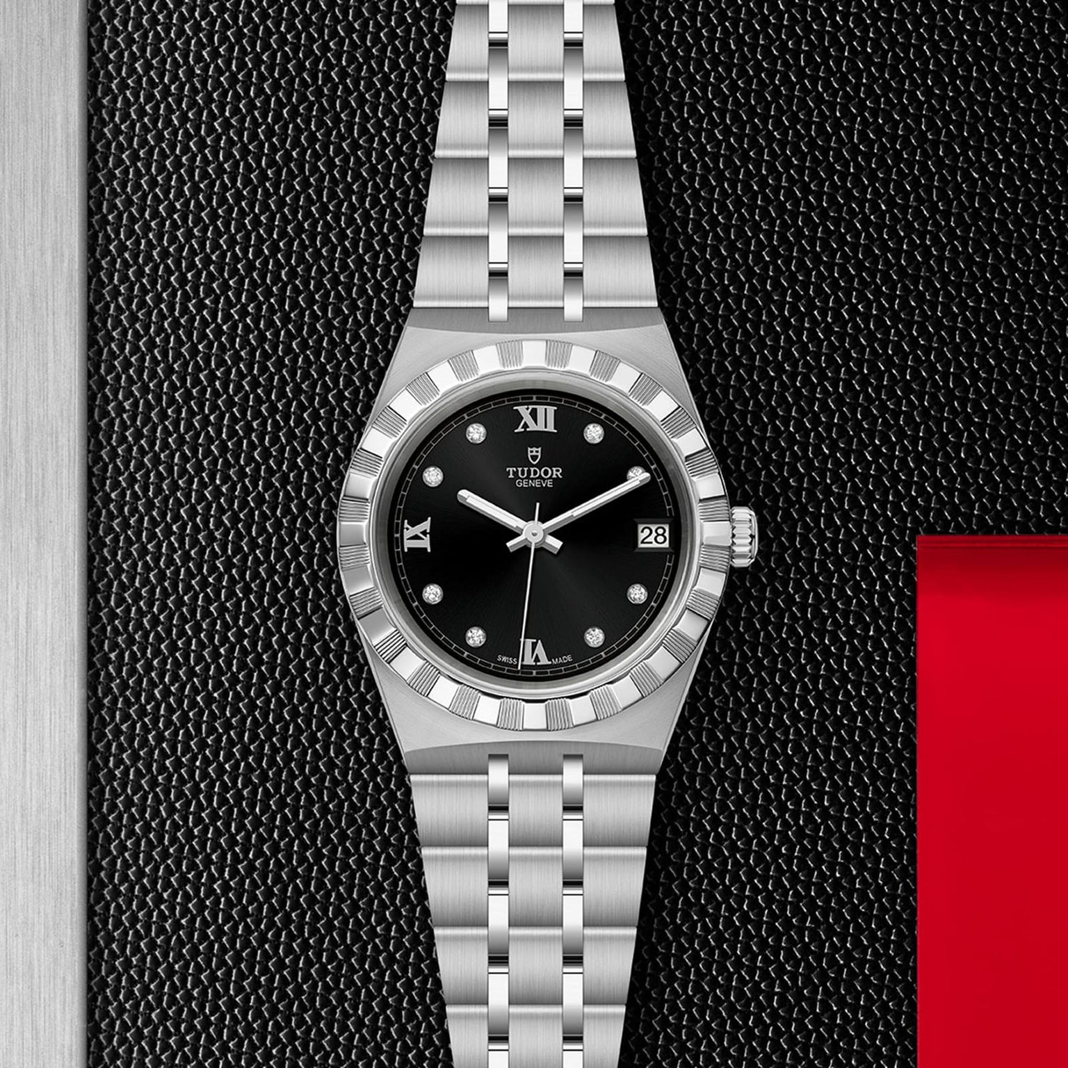 A TUDOR Royal wristwatch with a black dial, Roman numerals, diamond markers, date window, and integrated bracelet is displayed against a textured black and metallic backdrop.