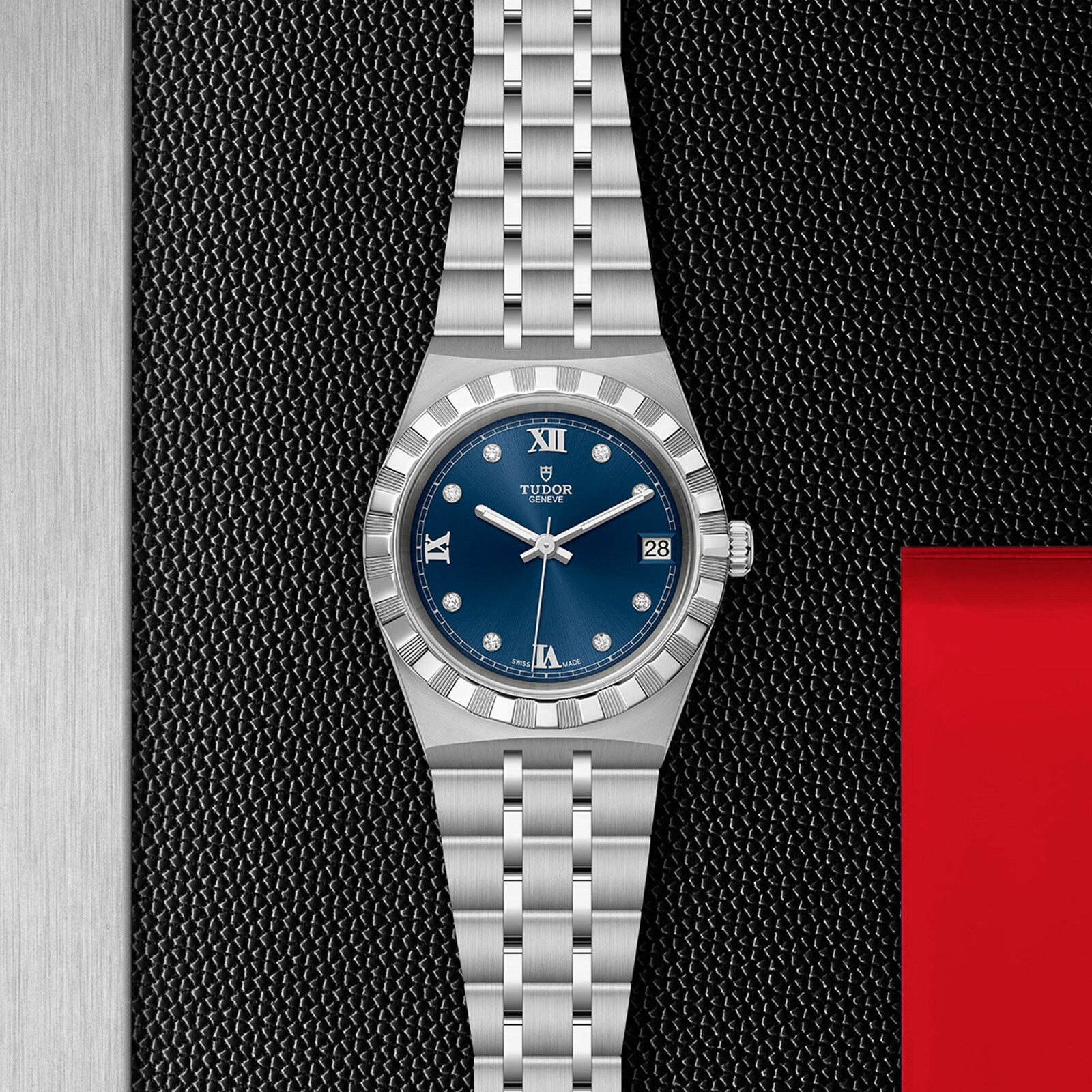 A TUDOR Royal stainless steel wristwatch with a blue dial, diamond hour markers, date display, and multi-link bracelet, photographed on textured black. Ideal for anyone seeking an automatic sport-chic timepiece.