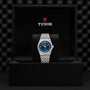 A TUDOR Royal wristwatch with a blue dial is showcased on a stand inside an open black Tudor watch box, highlighting the refined elegance of this automatic sport-chic timepiece.