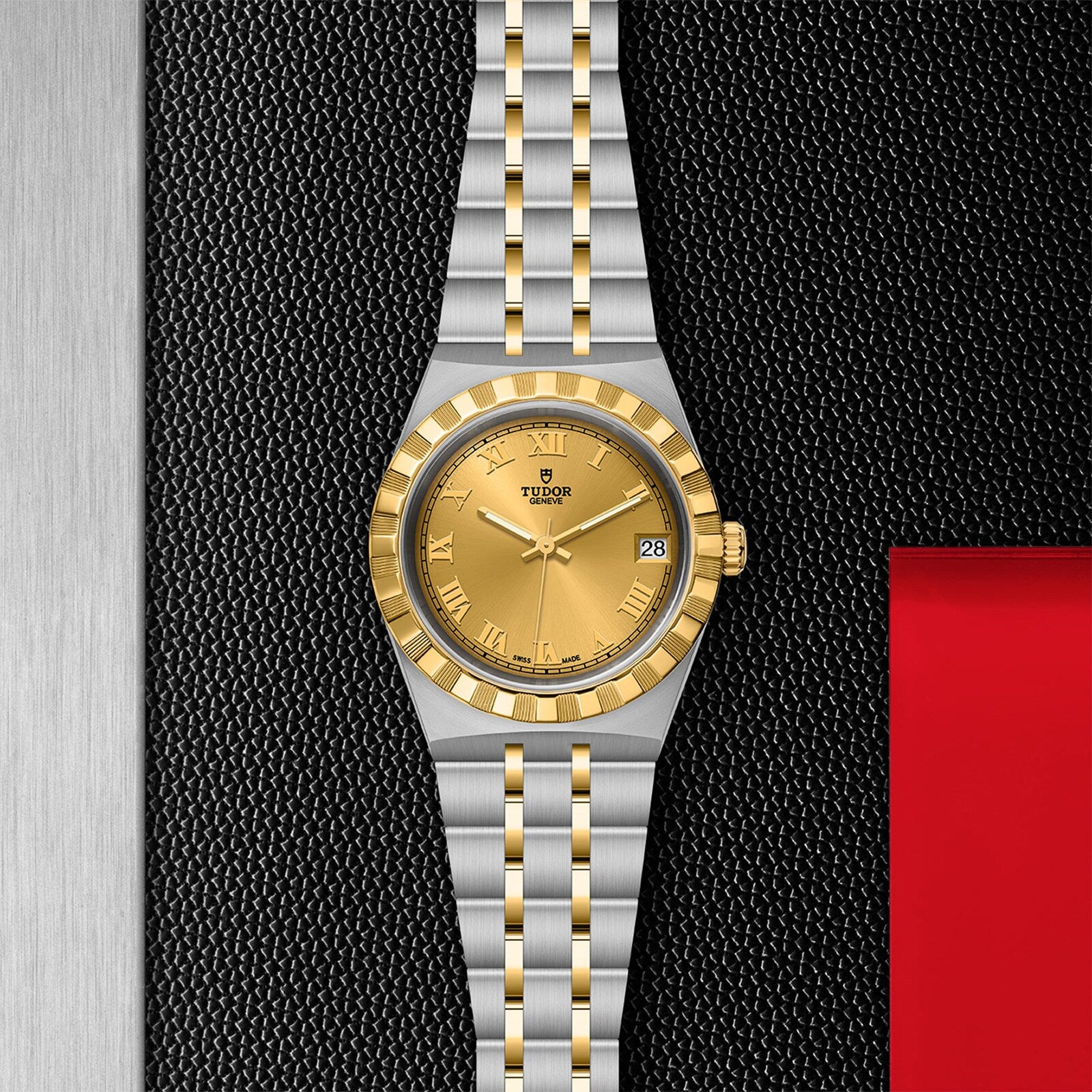 A TUDOR Royal wristwatch with a gold dial, Roman numerals, date display, and a stainless steel and gold bracelet is displayed on a textured black surface.