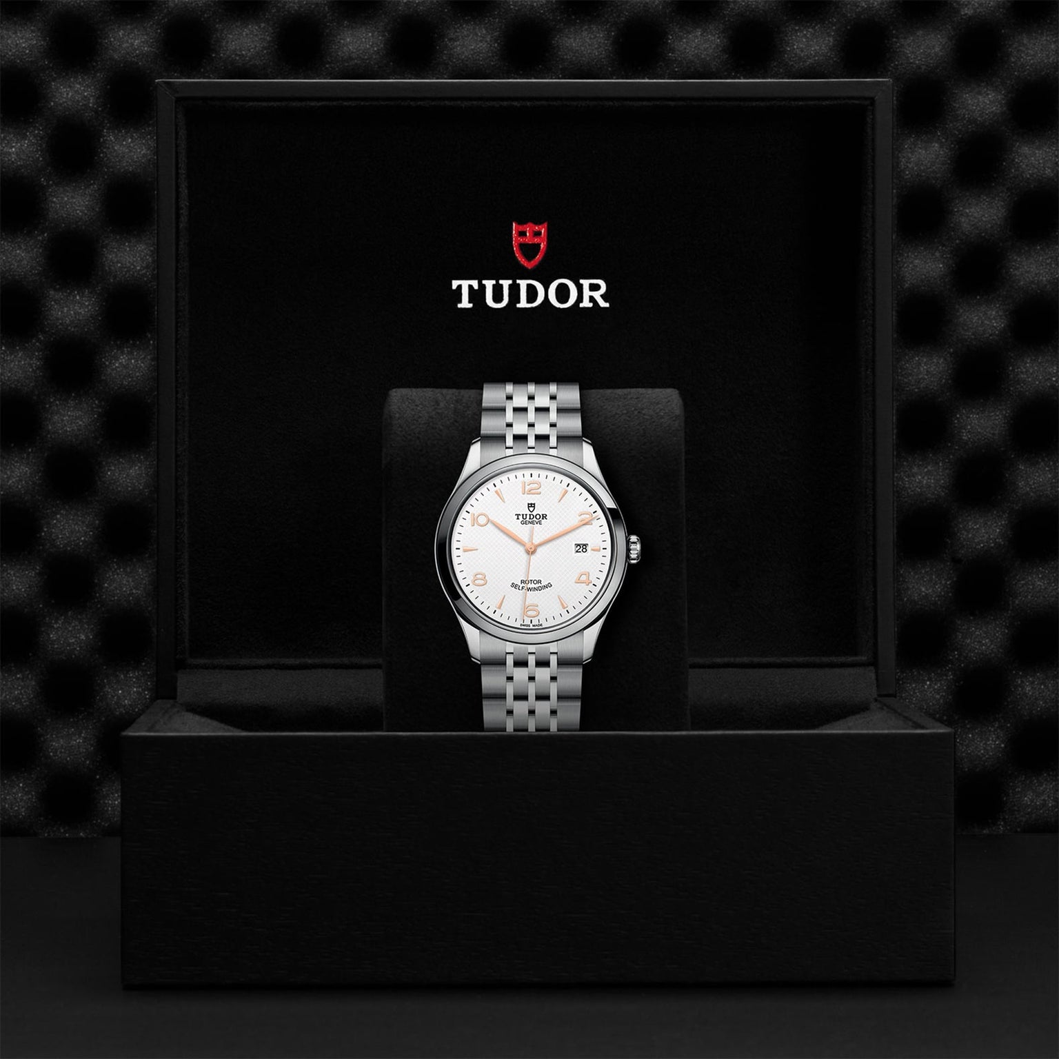 A TUDOR 1926 silver wristwatch with a white dial is displayed upright in an open black box featuring the TUDOR logo inside the lid—an elegant choice for any mechanical watch collection.