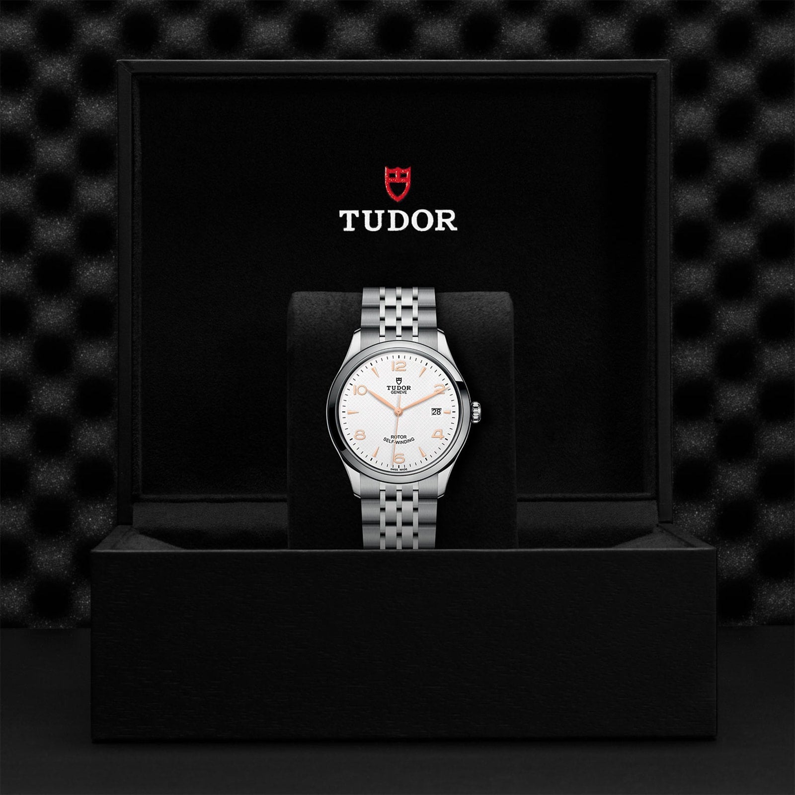 A TUDOR 1926 silver wristwatch with a white dial is displayed upright in an open black box featuring the TUDOR logo inside the lid—an elegant choice for any mechanical watch collection.
