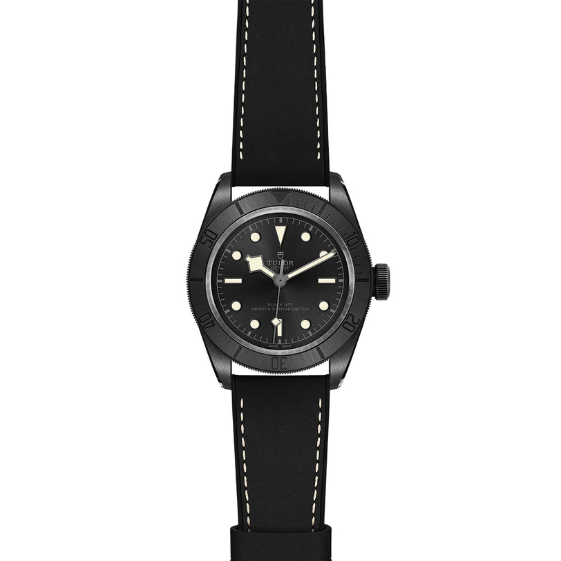 The TUDOR Black Bay Ceramic is a Swiss-made black wristwatch with a round case, black dial, luminous markers, black bezel, and a black leather strap with white stitching in classic Black Bay style.