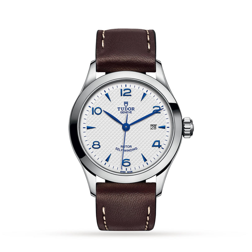The TUDOR 1926 features a white textured dial with blue numerals and hands, date display, stainless steel case, and brown leather strap—a classic mechanical wristwatch for timeless style.