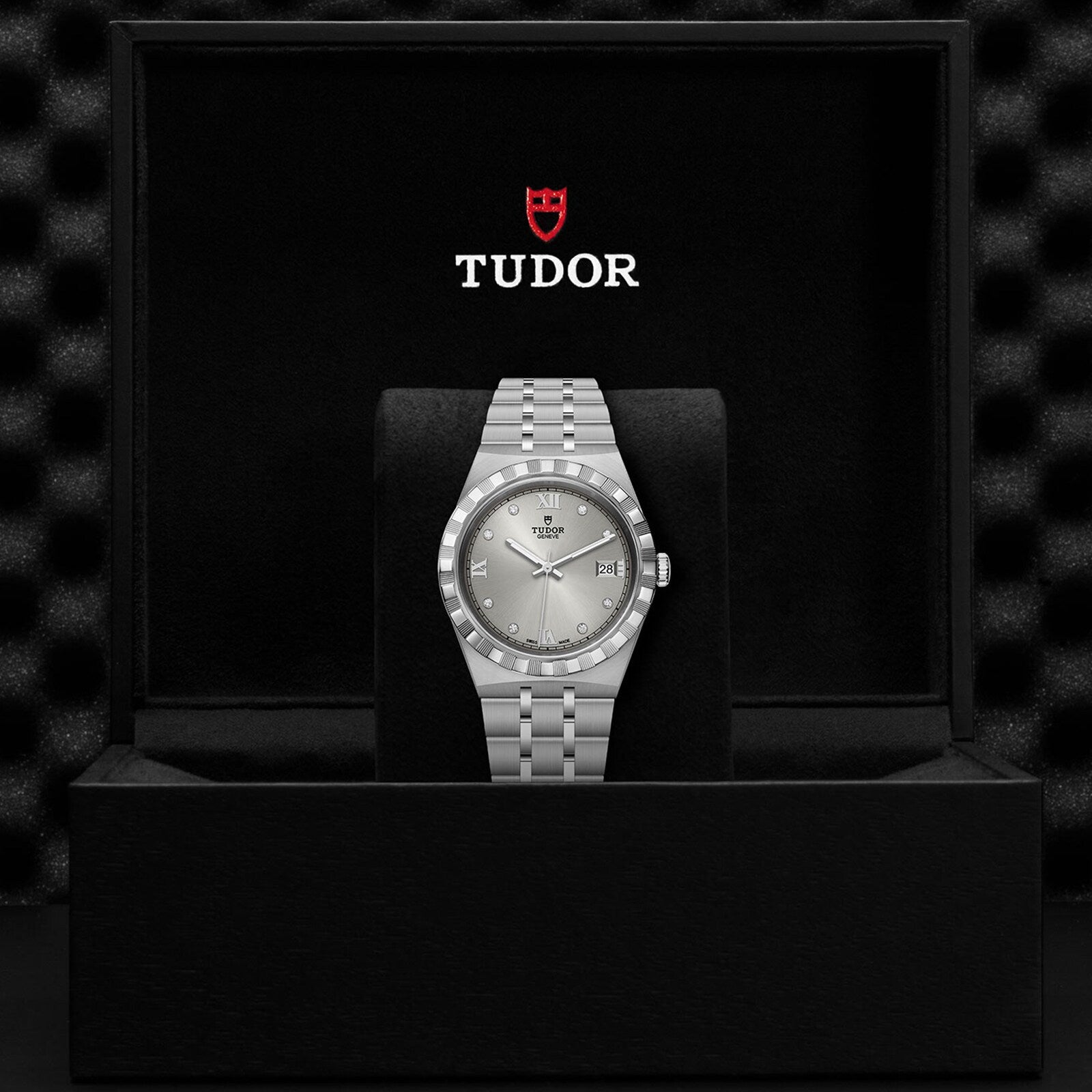 A TUDOR Royal wristwatch with a silver dial and integrated bracelet is presented in a black box featuring the Tudor logo, capturing the essence of TUDOR’s iconic automatic sport-chic watches.