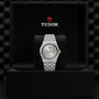 A TUDOR Royal wristwatch with a silver dial and integrated bracelet is presented in a black box featuring the Tudor logo, capturing the essence of TUDOR’s iconic automatic sport-chic watches.