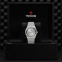 A TUDOR Royal wristwatch is upright in a black presentation box featuring the Tudor logo.