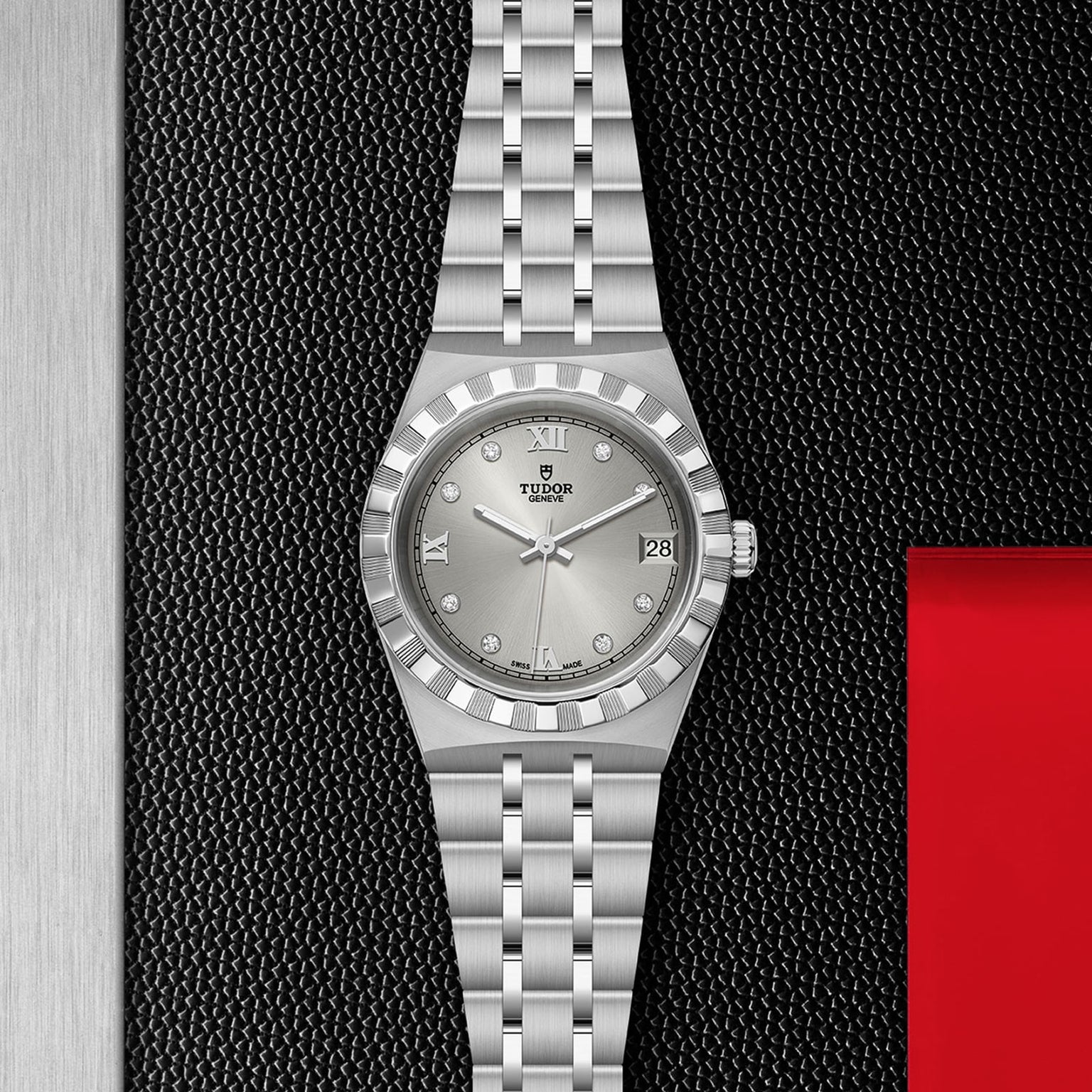 The TUDOR Royal, a silver wristwatch with metal bracelet, fluted bezel, diamond markers, and date display, is shown on a black and red textured background—a refined automatic sport-chic timepiece.