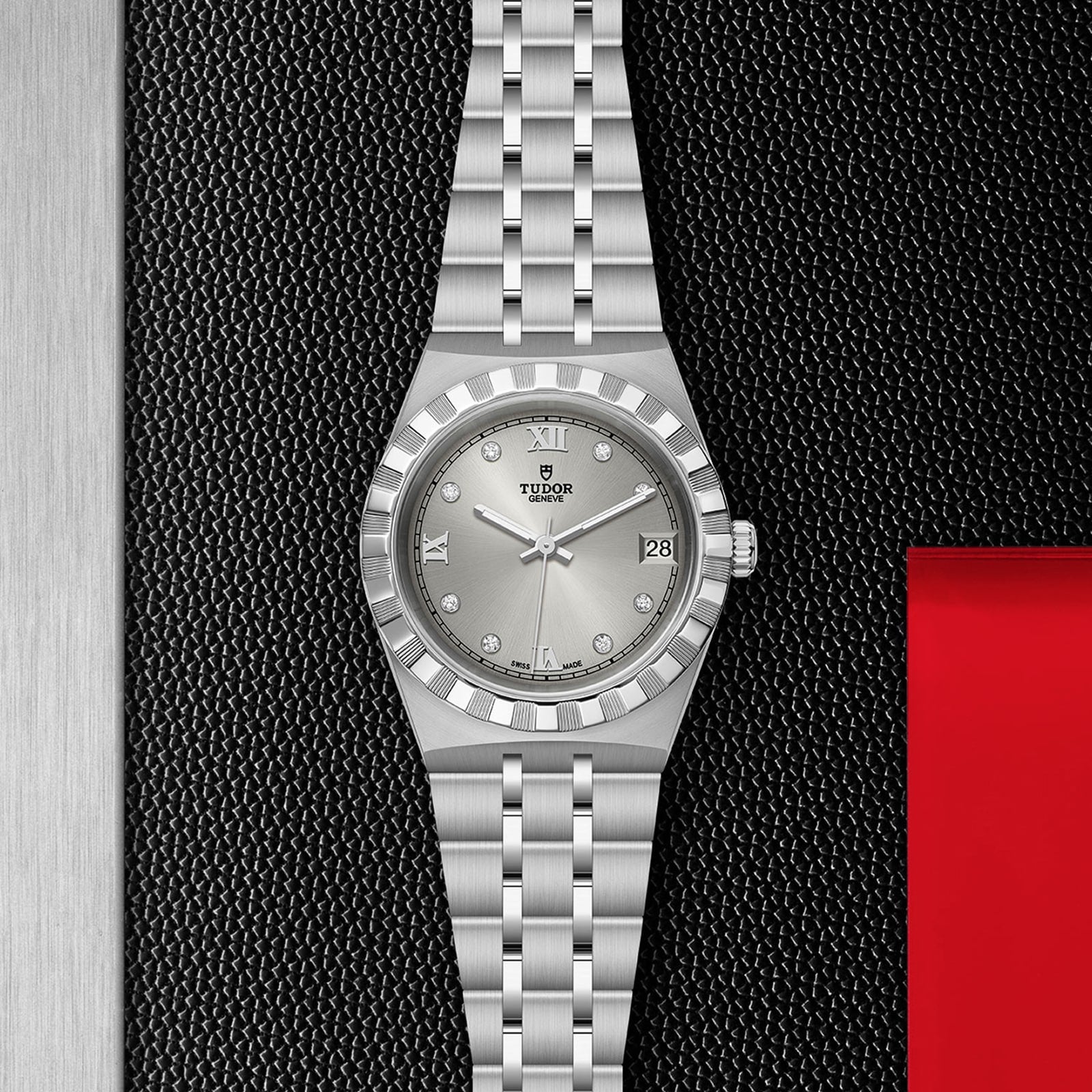 The TUDOR Royal, a silver wristwatch with metal bracelet, fluted bezel, diamond markers, and date display, is shown on a black and red textured background—a refined automatic sport-chic timepiece.