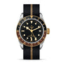 The TUDOR Black Bay GMT S&G features a black and gold bezel, black dial, gold crown, and a black fabric strap with a gold stripe. Its steel and gold design recalls classic TUDOR divers’ watches and includes a date at 3 o’clock.