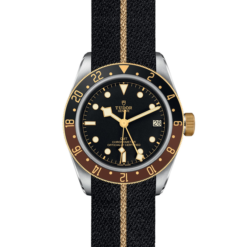 The TUDOR Black Bay GMT S&G wristwatch features a black and gold bezel, black dial, gold hour markers, and a black fabric strap with a gold stripe—a modern interpretation of classic Tudor divers’ watches in Steel & Gold.