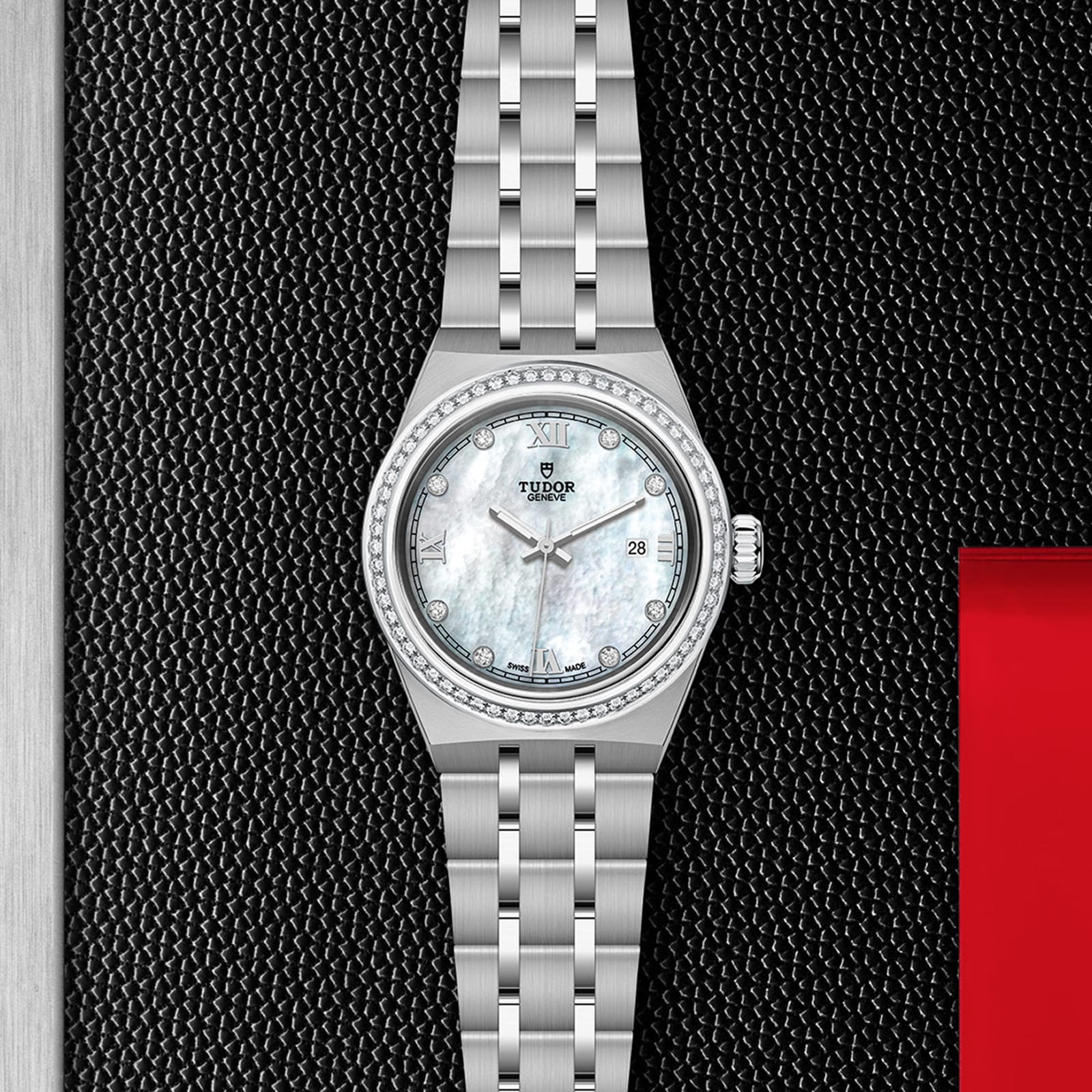 A stainless steel TUDOR Royal wristwatch with a mother-of-pearl dial, date display, and diamond bezel is shown on a textured black surface accented with red.