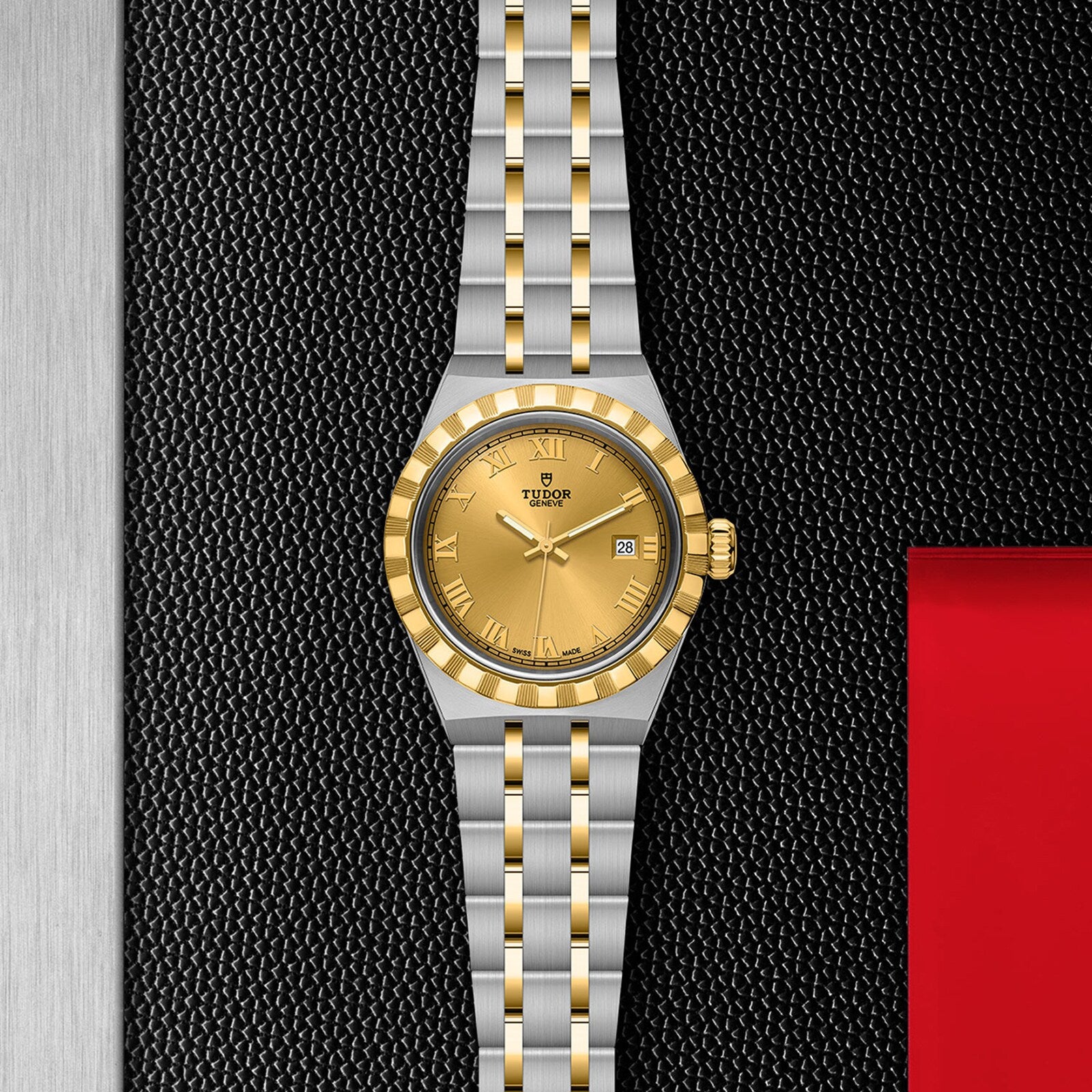 The TUDOR Royal wristwatch features a gold bezel, gold dial, stainless steel and gold bracelet, and a date window at 3 o’clock, set against a textured black and metallic background.