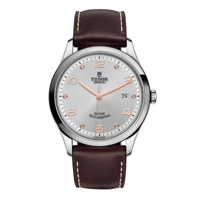 The TUDOR 1926 is a classic wristwatch featuring a silver dial, gold hour markers, mechanical movement, date at 3 o’clock, brown leather strap, and stainless steel case.